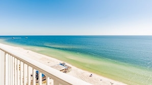 Uitzicht op een strand, met een heldere lucht, een pier die in het water verdwijnt en een zandstrand met enkele personen en gebouwen.
