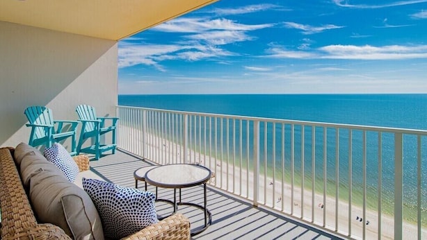 Een balkon met uitzicht op de oceaan, een bank, twee stoelen en een kleine tafel.