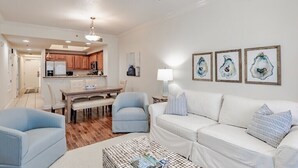 Een moderne woonkamer met een witte bank, blauwe fauteuils, een salontafel en kunst aan de muur.