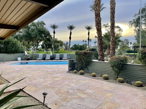 A pool area with stone flooring, lounge chairs, and palm trees.