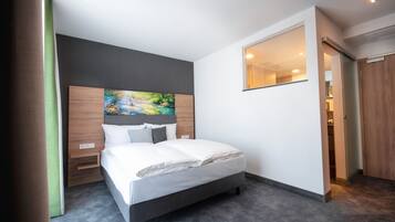 Quarto de hotel moderno com uma cama grande, um quadro na cabeceira, um espelho na parede e uma porta de madeira.