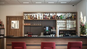 Eine Bar mit einer Holztheke, roten Stühlen und Regalen voller Flaschen und Gläsern.