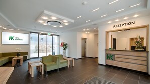 Ein Hotel-Empfangsbereich mit Empfangstresen, Sitzgelegenheiten und einem großen Bildschirm, der den Namen des Hotels zeigt.