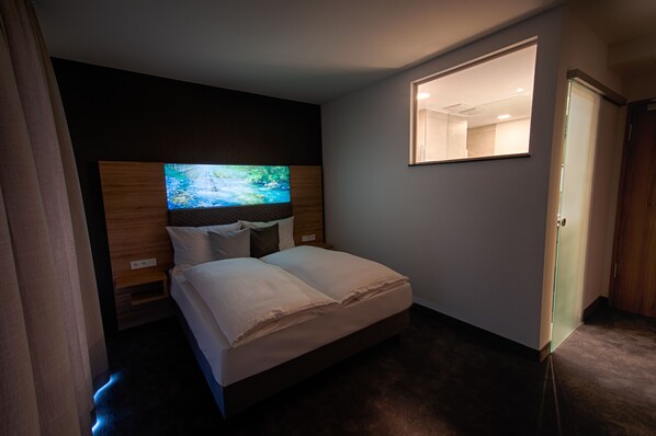 Una habitación de hotel con cama, televisión montada en la pared, espejo y puerta.