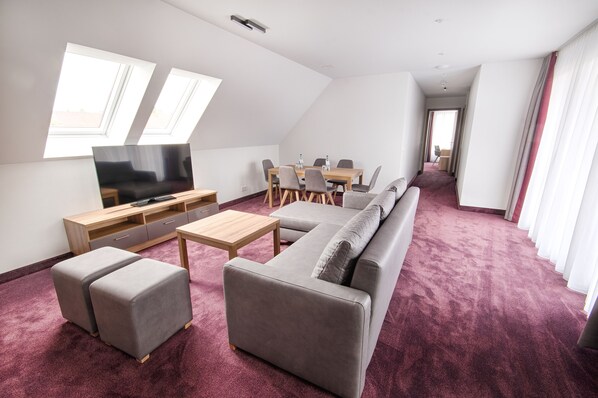 A modern living room with a sofa, ottomans, a TV, and a dining table. - Hotel Kupferzell (Kupferzell)