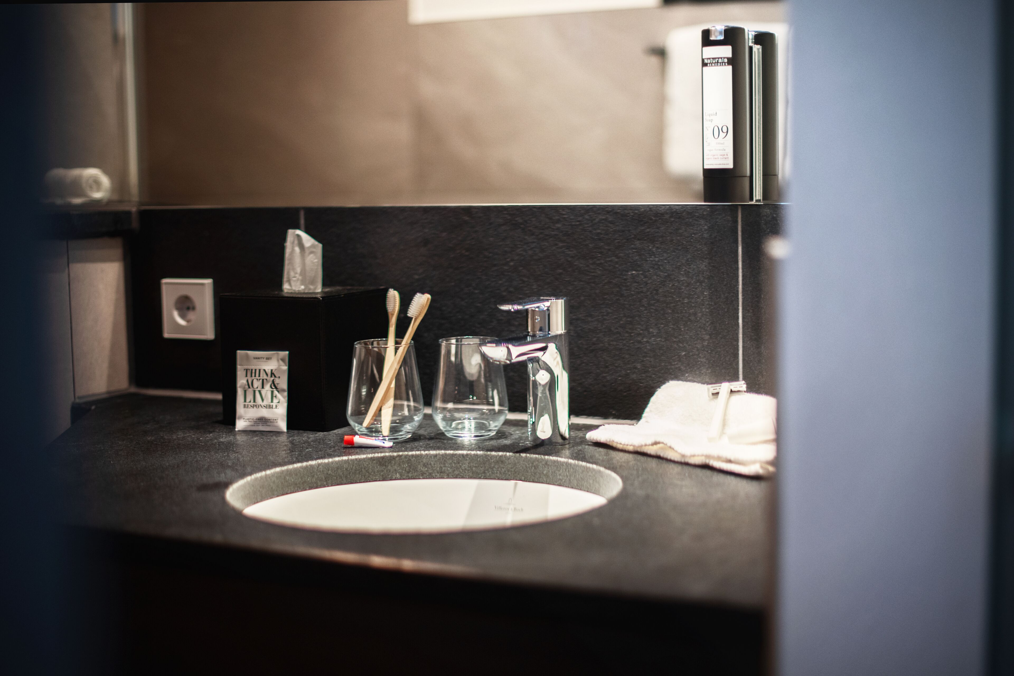 Un lavabo in bagno con uno specchio, spazzolini, un bicchiere e una scatola di fazzoletti.