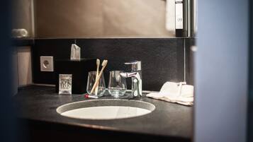 Un lavabo in bagno con uno specchio, spazzolini, un bicchiere e una scatola di fazzoletti.