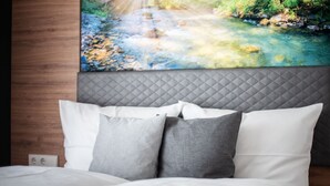 Ein Bett mit weißer und grauer Bettwäsche, ein gestepptes Kopfteil und ein Wandbild mit einer Flusslandschaft.