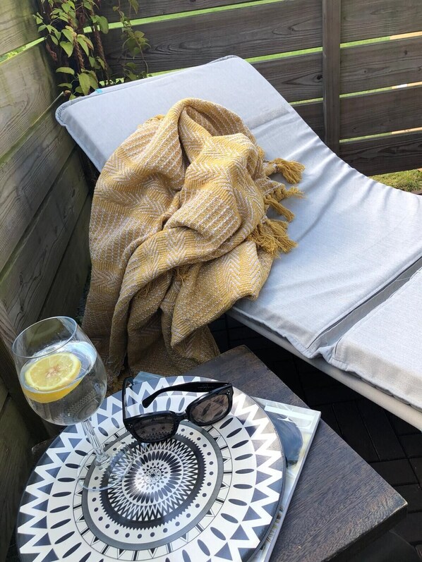 A sunbed with a yellow blanket, a glass of water with a lemon slice, and a pair of sunglasses on a patterned tray.