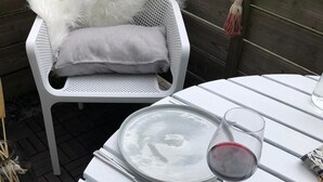 Une table de jardin blanche, avec une assiette, un verre à vin et un verre d’eau. Une paire de lunettes de soleil est posée sur la table.