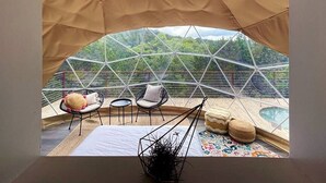 Una tienda en forma de domo geodésico con cama, dos sillones, una mesita y un jacuzzi.