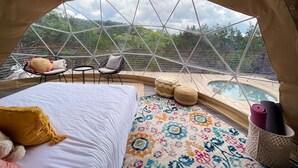 Alojamiento en tienda de campaña con una cama, una mesita, dos sillas y vistas a una piscina y un bosque.