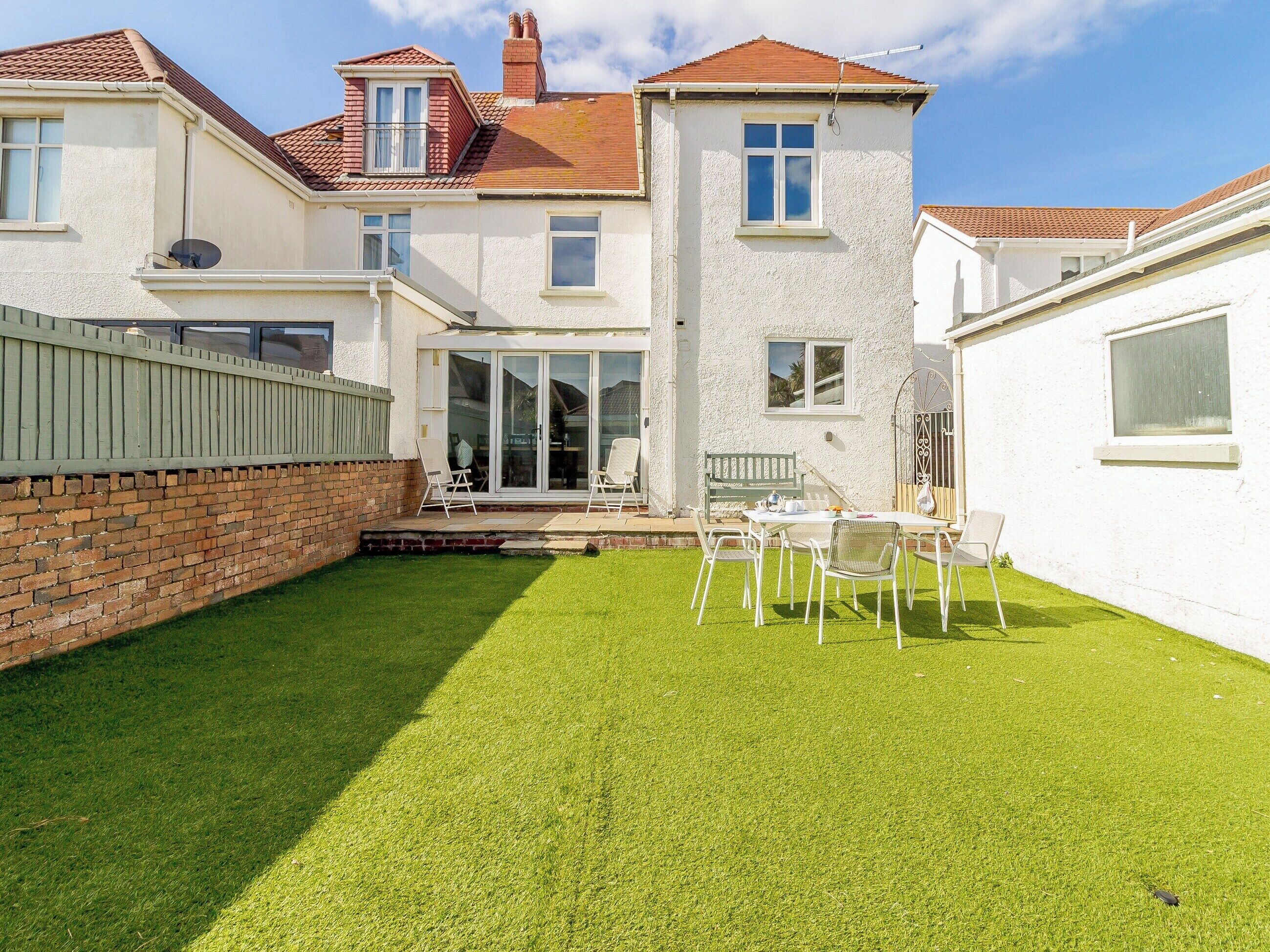 A two-story house with a patio area, a brick wall, and a well-maintained lawn.