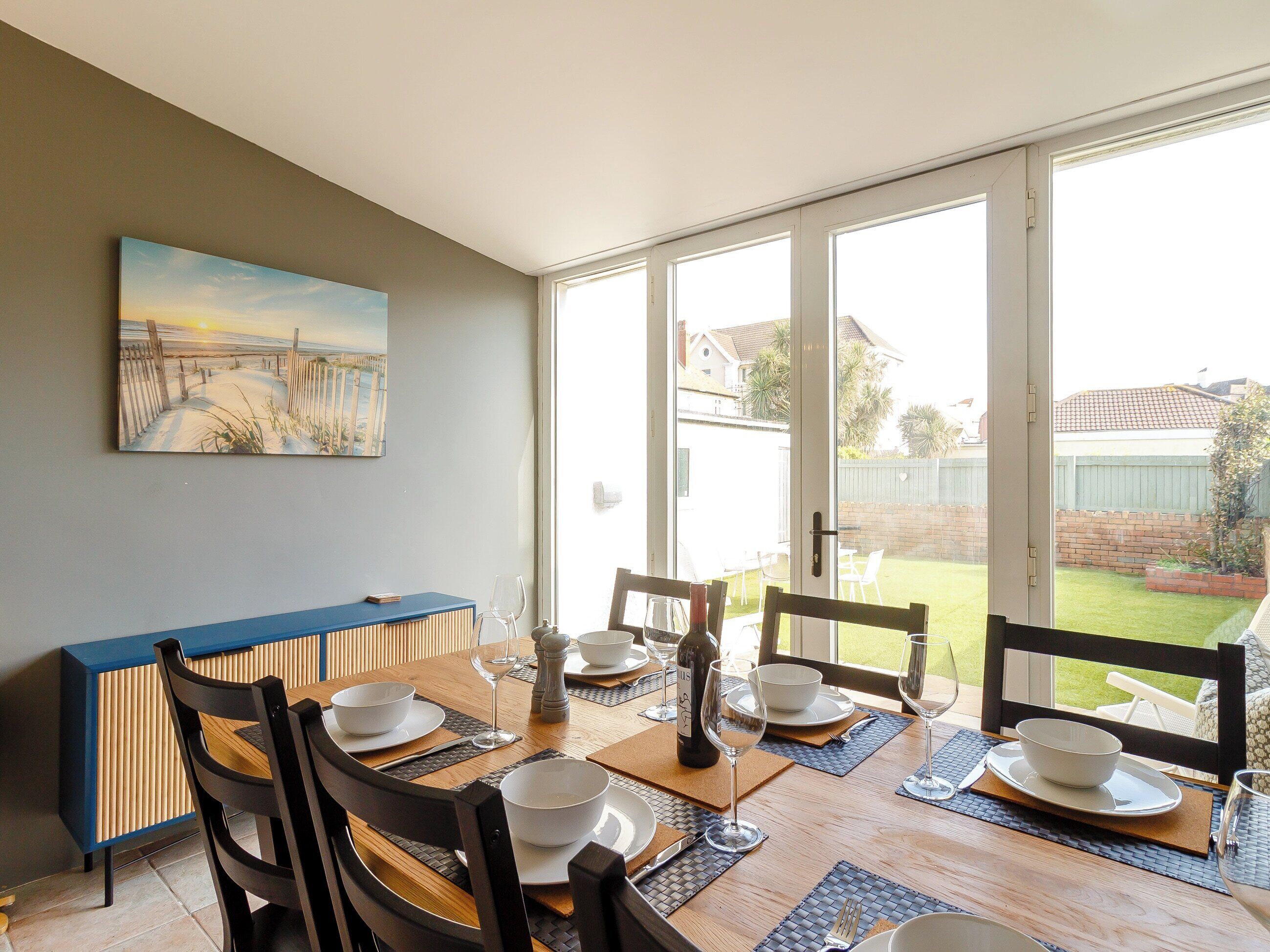 Un comedor con una mesa preparada para cuatro personas, un armario azul y un cuadro en la pared.