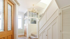 Un pasillo amplio con piso de madera, una escalera con candelabro y una puerta con paneles de vidrio emplomado.