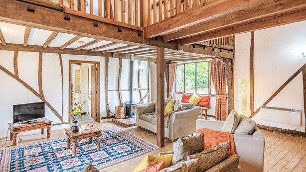 A rustic interior with exposed wooden beams, a fireplace, a sofa, and a television.