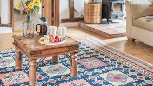 A cozy living room with a wooden coffee table, a vase of flowers, a coffee pot, and a rustic stove.