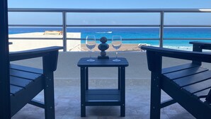 Un balcon avec une table et deux chaises, donnant sur une plage et l’océan.