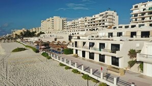 Un hôtel en bord de mer, avec plusieurs étages, une plage de sable en premier plan et un ciel bleu dégagé.