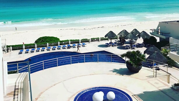 Un espace piscine d’un complexe hôtelier offrant une vue sur la plage et l’océan.
