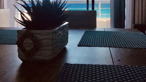 Une pièce dotée d’une grande fenêtre donnant sur une plage. On y trouve une plante sur une table et un tapis sur le sol.