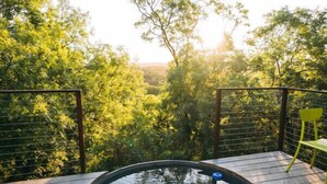 Un terrazza in legno con una vasca idromassaggio circolare immersa nel verde.