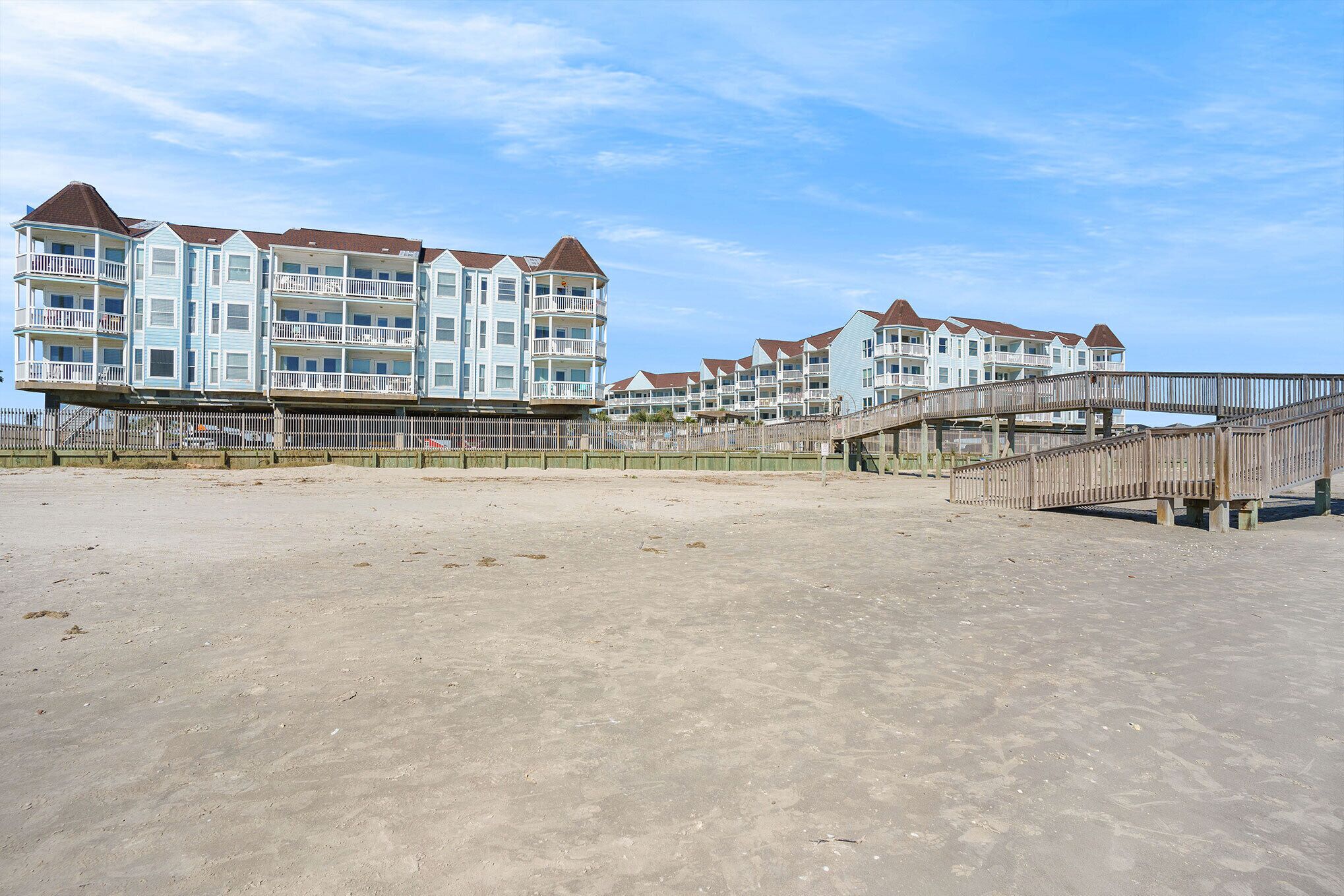 A beachfront hotel with multiple balconies, a wooden boardwalk, and a sandy beach.