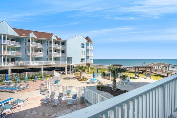 A beachfront hotel with multiple balconies, a pool area, and a boardwalk.