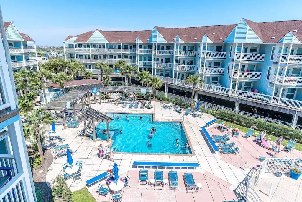 A hotel with a large pool area, multiple balconies, and a view of the surrounding landscape.