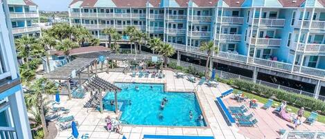 A hotel with a large pool area, multiple balconies, and a view of the surrounding landscape.