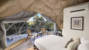 Ein gemütliches Zelt mit Bett, kleinem Tisch und Stuhl. Ein Fenster bietet einen Ausblick auf eine schöne Landschaft.