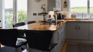A kitchen with a wooden island, bar stools, a clock, a coffee maker, and a view of the outdoors. - A lovely welcoming house with all the comforts of home. (Morfa Bychan)