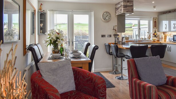 A dining area with a view, a kitchen with a clock, and a living room with a fireplace. - A lovely welcoming house with all the comforts of home. (Morfa Bychan)