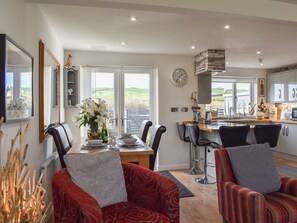 A dining area with a view, a kitchen with a clock, and a living room with a fireplace. - A lovely welcoming house with all the comforts of home. (Morfa Bychan)