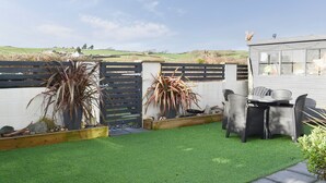 A backyard with artificial grass, a wooden fence, and outdoor furniture. - A lovely welcoming house with all the comforts of home. (Morfa Bychan)
