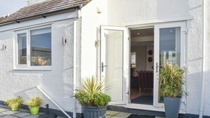 A residential house with a white exterior, a sliding glass door, and potted plants on the front. - A lovely welcoming house with all the comforts of home. (Morfa Bychan)