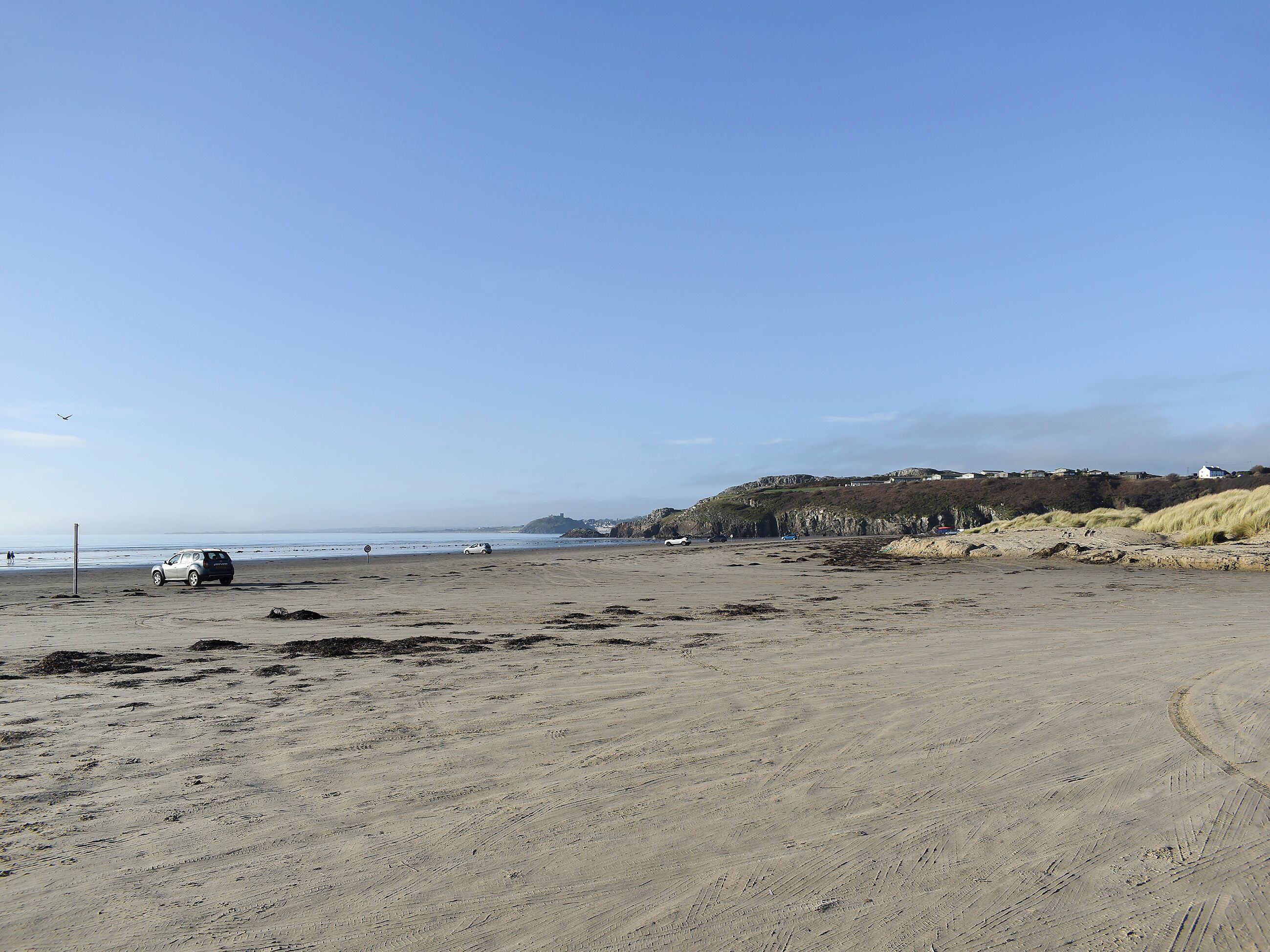 Une plage de sable avec quelques voitures et une colline qui se dessine à l’horizon.