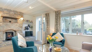 A cozy living room with a stone fireplace, teal sofas, a glass coffee table, and a view of the outdoors through a window. - 2 bedroom accommodation in Modbury (Modbury)