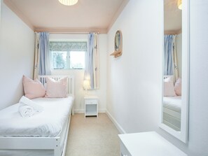 Une chambre avec deux lits, une table de chevet avec une lampe, un miroir et une fenêtre avec des rideaux.