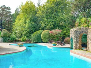 Une piscine agrémentée d’une arche en pierre, entourée d’une végétation luxuriante et de tables de pique-nique.