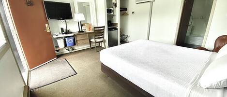 Une chambre d’hôtel avec un grand lit, un bureau avec une chaise, une télévision et une armoire.