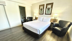 Quarto de hotel com uma cama grande, uma cadeira, uma mesinha de cabeceira e duas luminárias fixadas na parede.
