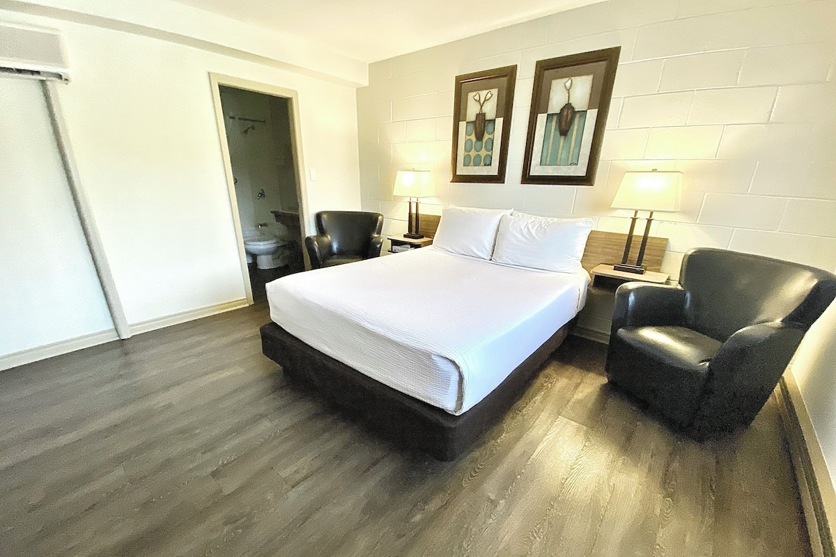 A hotel room with a large bed, a chair, a nightstand, and two wall-mounted lamps.