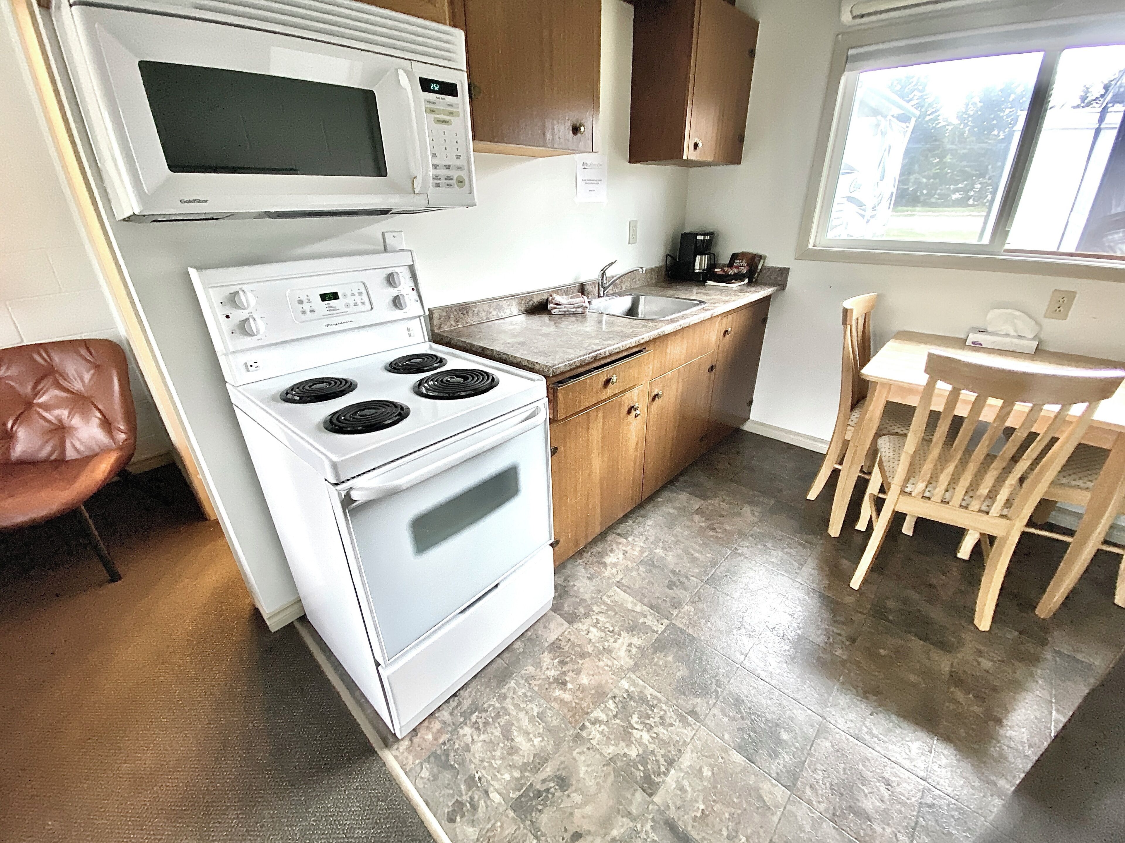 A compact kitchen with a stove, microwave, and sink, wooden cabinets, and a dining area with a table and chairs.