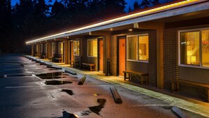 Fileira de quartos de motel com entradas individuais, galeria coberta e estacionamento com buracos visíveis.