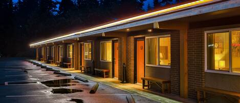 A row of motel rooms with individual entrances, a covered walkway, and a parking lot with visible potholes.