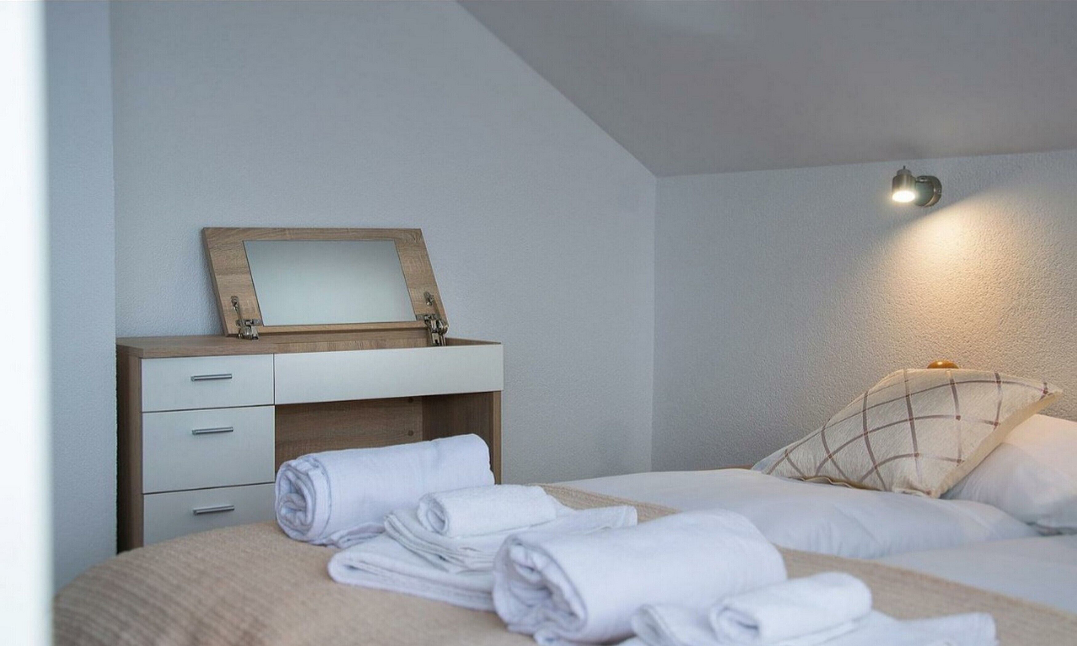 Un dormitorio con una cama, una mesita de noche con espejo y una lámpara de pared.