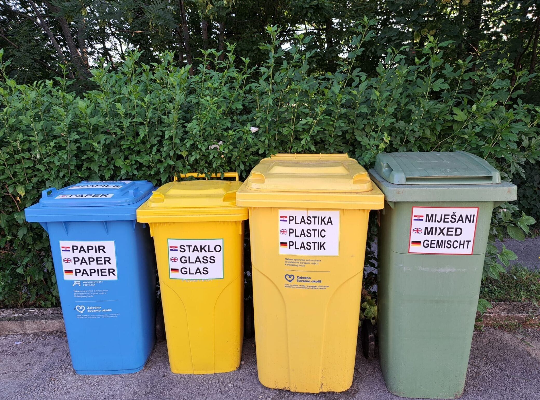Vier afvalbakken, aangeduid voor papier, glas, plastic en restafval.