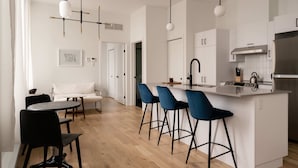 A modern kitchen with a central island, bar stools, and a dining area with a table and chairs. - Maison Rasco by Luxury In Transit (Montreal)