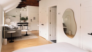 A modern, well-lit room with a wooden ceiling, a round mirror, a bed, a sofa, and a small table. - Maison Rasco by Luxury In Transit (Montreal)